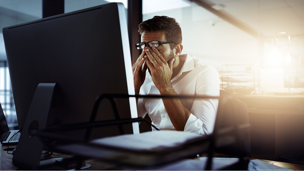 A frustrated business owner rubbing his eyes while looking at a computer screen, symbolizing the stress of having a new website that is invisible on Google search results.